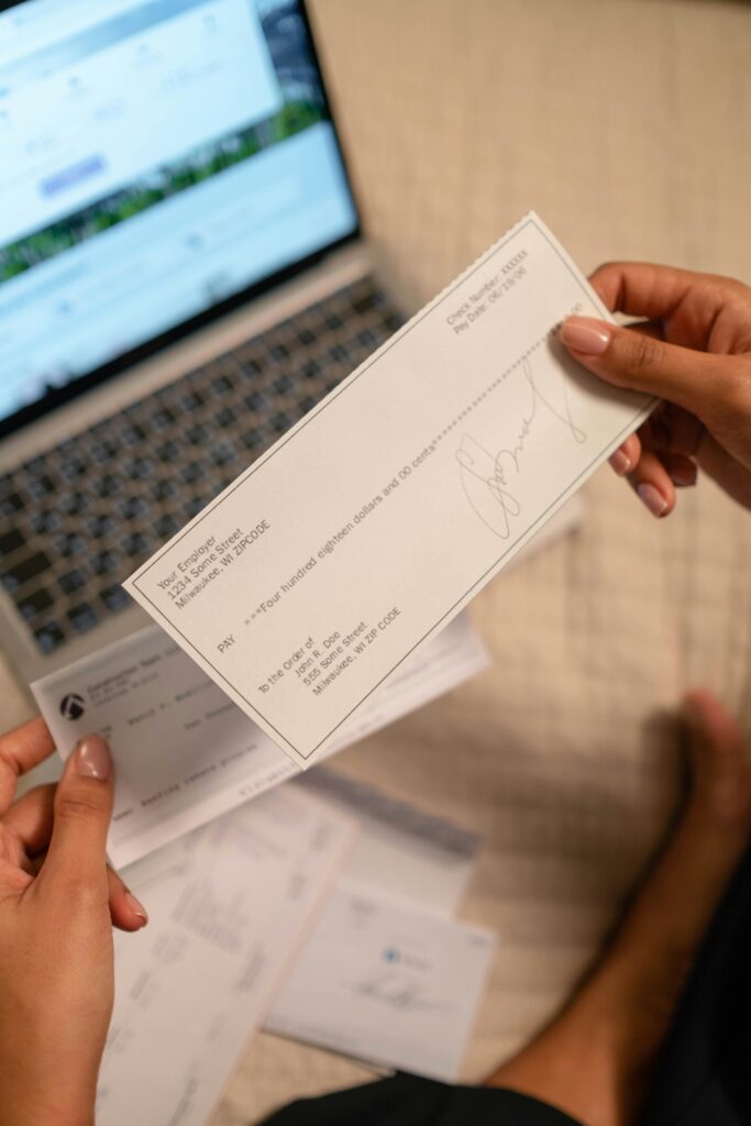 Individual holding a cheque over laptop, signifying online banking or financial transaction.